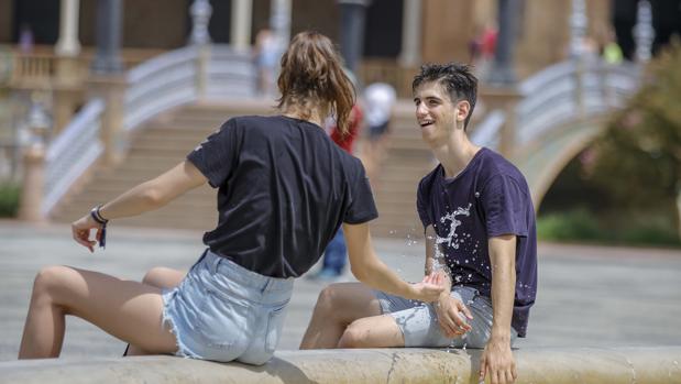 Dos jóvenes se refrescan en la Plaza de España de Sevilla